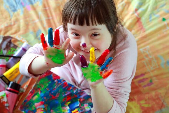 Smiling girl with down syndrome painting with hands