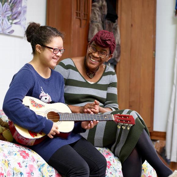 Smiling health carer with young woman playing guitar